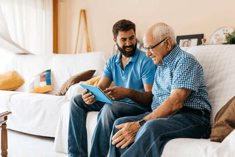 Young man showing an older man something on a tablet, sitting on a couch.