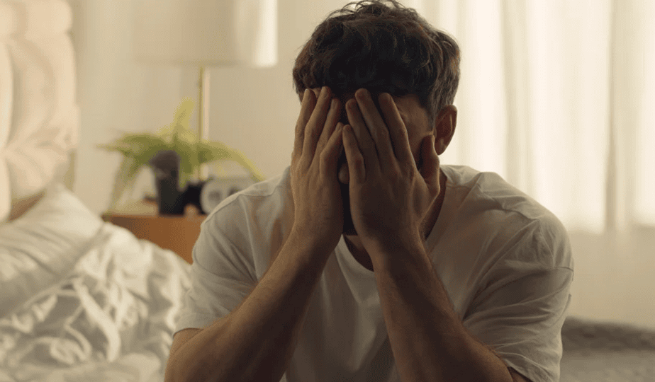 Man sitting on bed with face in hands, struggling with alcohol and mental health.