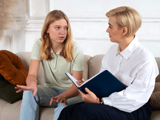 Teen girl talks to a therapist during psychiatric evaluations, who takes notes.