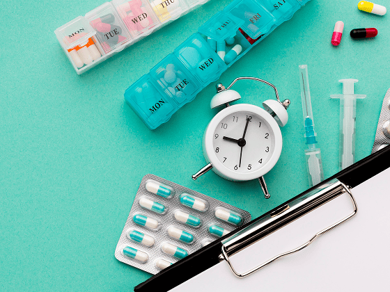 Medication management psychiatry: Pills, alarm clock, and clipboard for organizing medicine schedule.