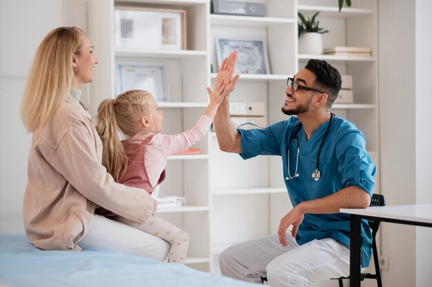 Girl and doctor high-fiving in clinic with mother present. Positive healthcare experience.
